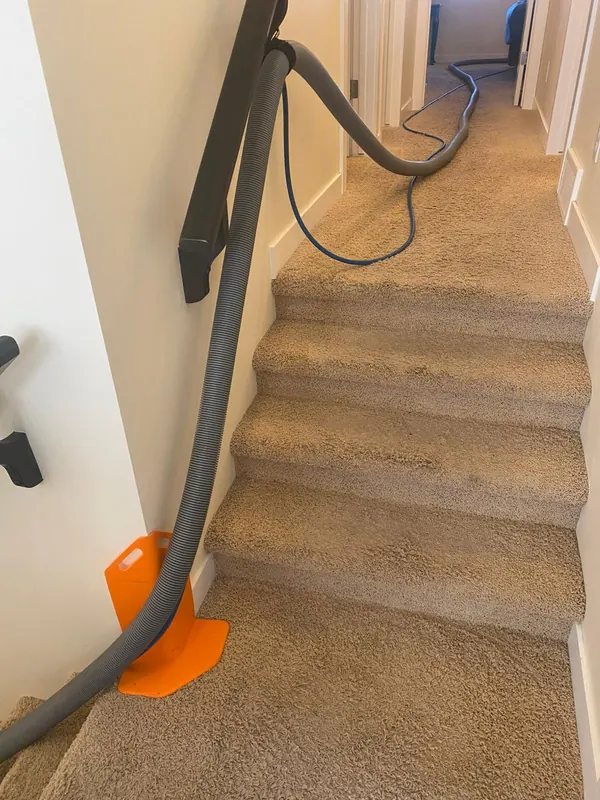 Cleaning hoses running up a carpeted staircase, with an orange corner guard protecting the wall at the bottom